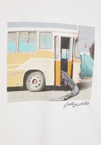 Retro žlto-biely autobus s otvorenými dverami a veľkým chvostom krokodíla, ktorý presahuje na chodník vonku.