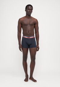 Bóxer negro para hombre, confeccionado en tela suave, con una cinturilla de contraste que muestra el nombre de la marca y rayas rojas y blancas.