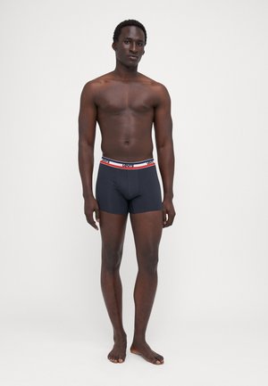Caleçons noirs pour hommes en tissu lisse, avec une ceinture contrastante portant le nom de la marque et des rayures rouges et blanches.