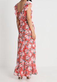 Maxi šaty z červené látky, zdobené květinovým vzorem s bílými a modrými květy, s volánovými rukávy a nařaseným lemem.