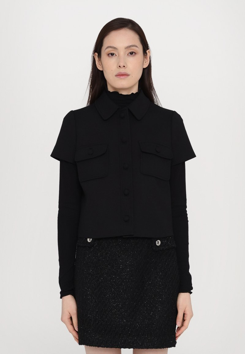 Cropped black jacket with short sleeves, front buttons, and two chest pockets; paired with a textured black skirt featuring metallic accents.