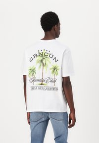 Hvid bomulds-T-shirt med grafikdesign af palmer og teksten "CANCUN Paradis Club" samt feriestedets detaljer i sort og grøn.