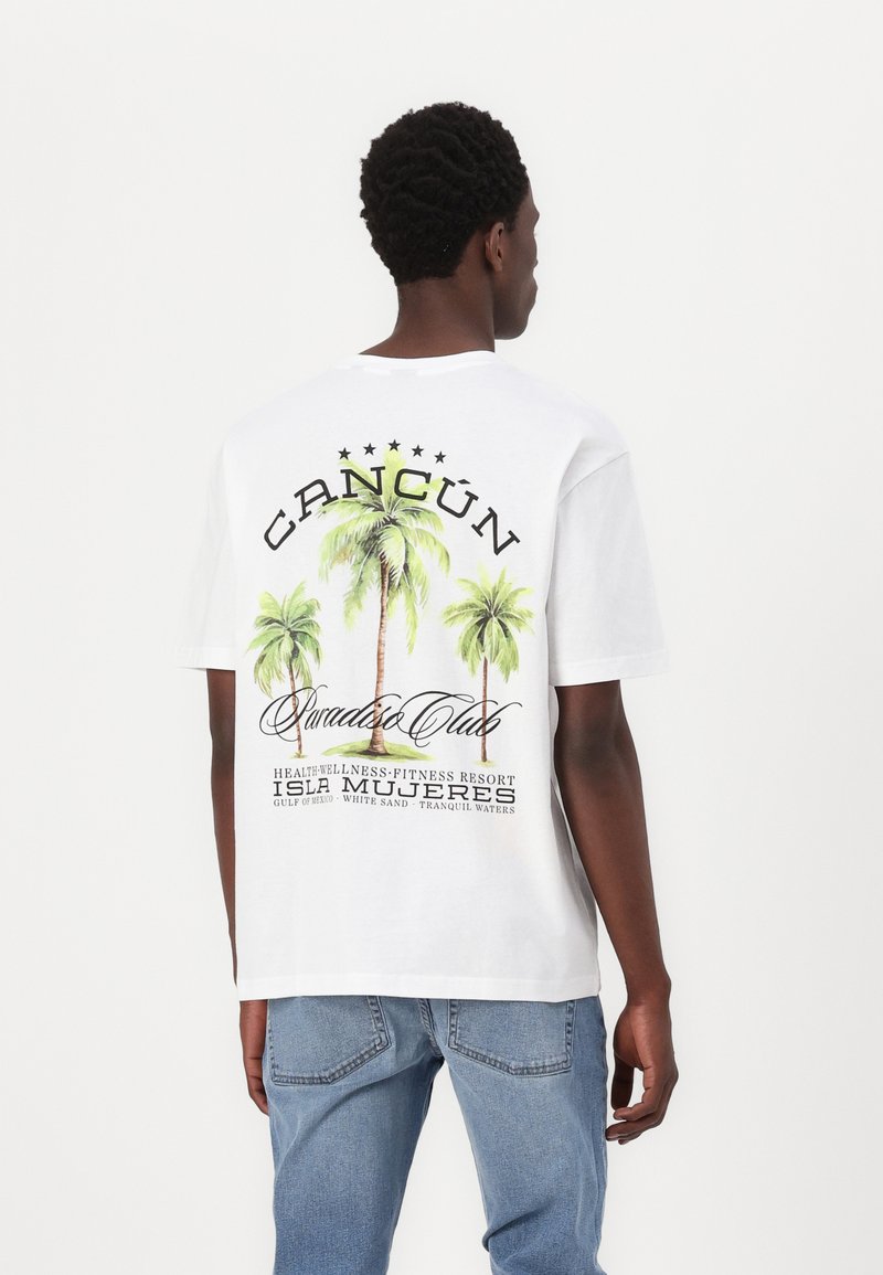 Hvid bomulds-T-shirt med grafikdesign af palmer og teksten "CANCUN Paradis Club" samt feriestedets detaljer i sort og grøn.