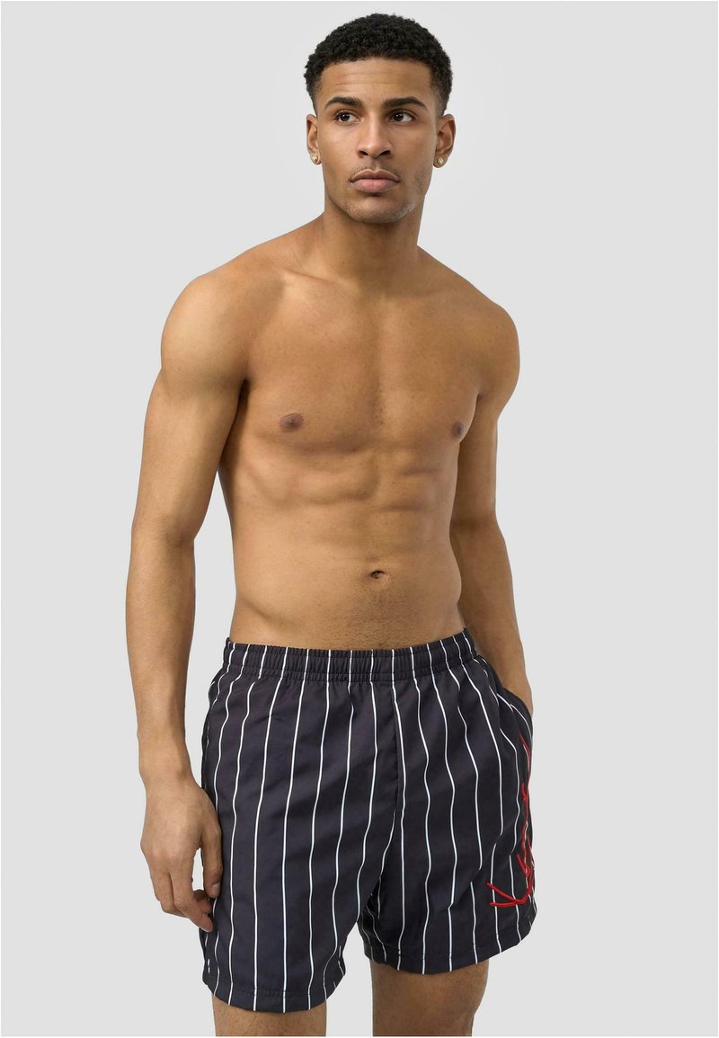 Shorts de bain rayés bleu marine avec des lignes verticales blanches et un accent rouge, dotés d'une taille élastique et de poches latérales, fabriqués en tissu léger.