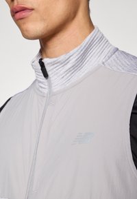 Šviesiai pilkas užsegamas švarkas su gofruotu apykakliu, juodais akcentais ir subtiliu logotipu. Lygus audinys ir minimalistinis dizainas.