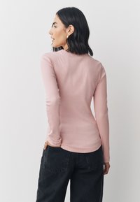 Long-sleeve, ribbed top in soft pink fabric with a round neck. Paired with high-waisted black wide-leg pants, showing a relaxed fit.