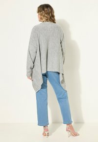 Cardigan grigio a maglia con orlo posteriore lungo, abbinato a jeans a gamba dritta azzurri e sandali argentati con tacco alto. Materiale testurizzato.