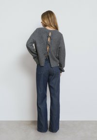 Suéter de punto gris con un diseño de espalda descubierta, atado con cintas. Combinado con pantalones de campana de rayas azul oscuro, con cintura alta.