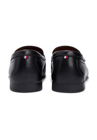 Μαύρα δερμάτινα μοκασίνια με λεία υφή, χαμηλό προφίλ και αντίθετες κόκκινες, λευκές και μπλε λεπτομέρειες κοντά στη φτέρνα.