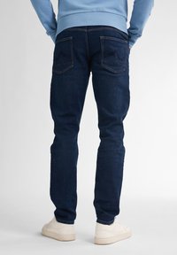 Vaqueros azul oscuro con un corte ajustado, que cuentan con bolsillos traseros y detalles de costura sutiles. Combinados con un sudadera de color azul claro y zapatillas blancas.