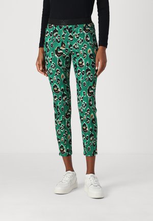 Green patterned pants with a black elastic waistband, featuring leopard print designs in black, gold, and dark green, complemented by white sneakers.