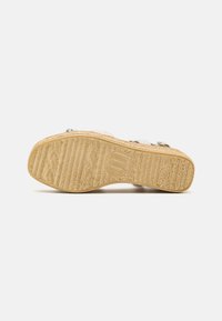 Woven straw sole with a textured rubber bottom; light beige color with a soft, smooth upper. Notable embossed logo in the center.