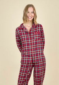 Punane ruudulise mustriga pidžaama komplekt, mis sisaldab nööpidega ülemist osa koos krae ja taskuga, ning sobivaid pükse. Pehme kangas, millel on ruuduline muster.