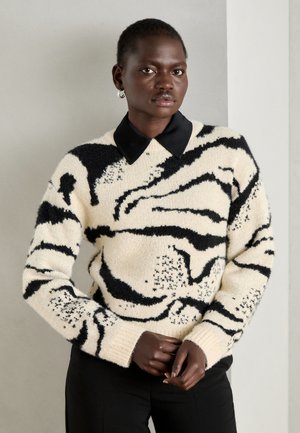 Pull en maille crème avec motif abstrait noir, doté d'un col noir, de manches longues et de poignets côtelés.