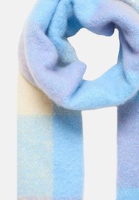 Sciarpa dalla consistenza morbida con ampi blocchi pastello in azzurro chiaro, lavanda e crema, disposta allentatamente su uno sfondo bianco.