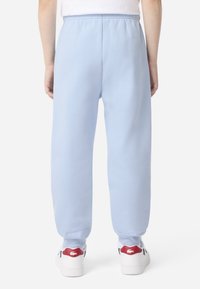 Svetlomodré tepláky s voľným strihom, elastickým pásom a zúženými členkami, v kombinácii s bielymi teniskami s červenými detailmi.