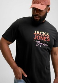 Juodas trumpomis rankovėmis marškinėliai su "JACK & JONES" gradientinės oranžinės iki geltonos spalvos spauda, papildyta rožiniu parašu.