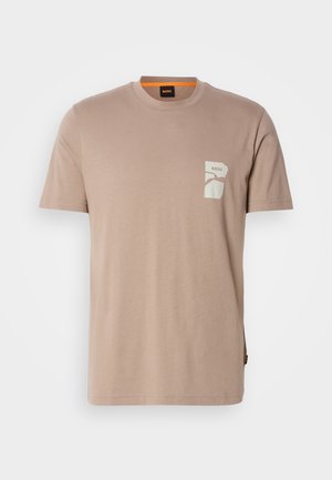 T-shirt beige in cotone con collo rotondo, maniche corte e una patch rettangolare bianca con la parola "BOSS" e forme astratte.