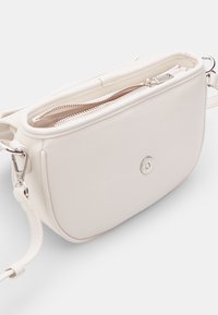 Biała skórzana torba na ramię o gładkiej fakturze, z kieszeniami zapinanymi na zamek i srebrnymi akcesoriami. Posiada okrągły kształt i subtelne logo.