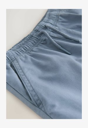 Gaiši zili šorti no mīksta auduma, ar elastīgu jostasvietu, kurai pievienota aukla, un sānu kabatām. Gluda tekstūra, ikdienišķs dizains.