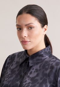 Blusa scura a fantasia realizzata in tessuto liscio, con collo, bottoni e una sottile stampa leopardata nelle tonalità di nero e grigio.