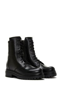 Bottes en cuir noir à lacets avec une fermeture éclair latérale, une semelle épaisse et des œillets circulaires. Caractérisées par un matériau texturé et un design robuste.