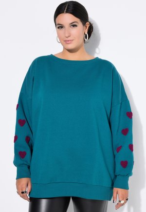 Turkusowy, oversize sweter z długimi rękawami, z bordowymi dodatkami w kształcie serca na obu rękawach. Miękki materiał, luźny krój, ściągacz na dole.