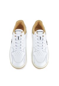 Zapatillas deportivas blancas con un empeine de cuero liso, detalles en color marrón claro en el cuello, caja de puntera perforada y logotipo negro en el costado.