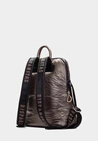 Mochila acolchada en gris metálico con detalles en negro. Cuenta con correas ajustables con logotipo, cierre de cremallera y un asa superior. Textura suave.