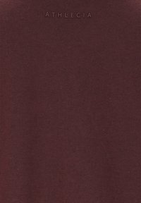 Bordeauxfarbiges T-Shirt aus weicher Baumwolle, mit einer glatten Textur und dem geprägten Markennamen "ATHLECIA" nahe dem Ausschnitt.