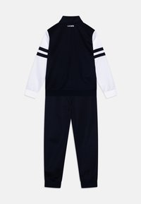 Dres Lacoste w kolorze granatowym i białym, z wysokim kołnierzem, paskami na rękawach oraz elastycznymi mankietami. Miękki materiał z sportowym designem.