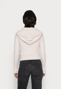 Light pink ribbed knit hoodie with a large, folded collar and a relaxed fit, paired with dark gray slim-fit jeans.