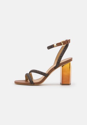 Sandale à talon haut marron avec talon bloc doré, deux fines brides en tissu sur le pied, et une bride de cheville avec boucle dorée et clou.