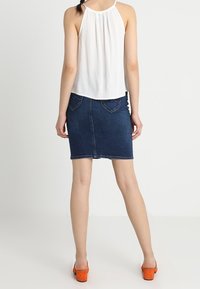 Biała bluzka na halter i ciemnoniebieska spódnica dżinsowa, z dopasowanym krojem i kieszeniami oraz pomarańczowe platformy. Gładka tekstura całości.