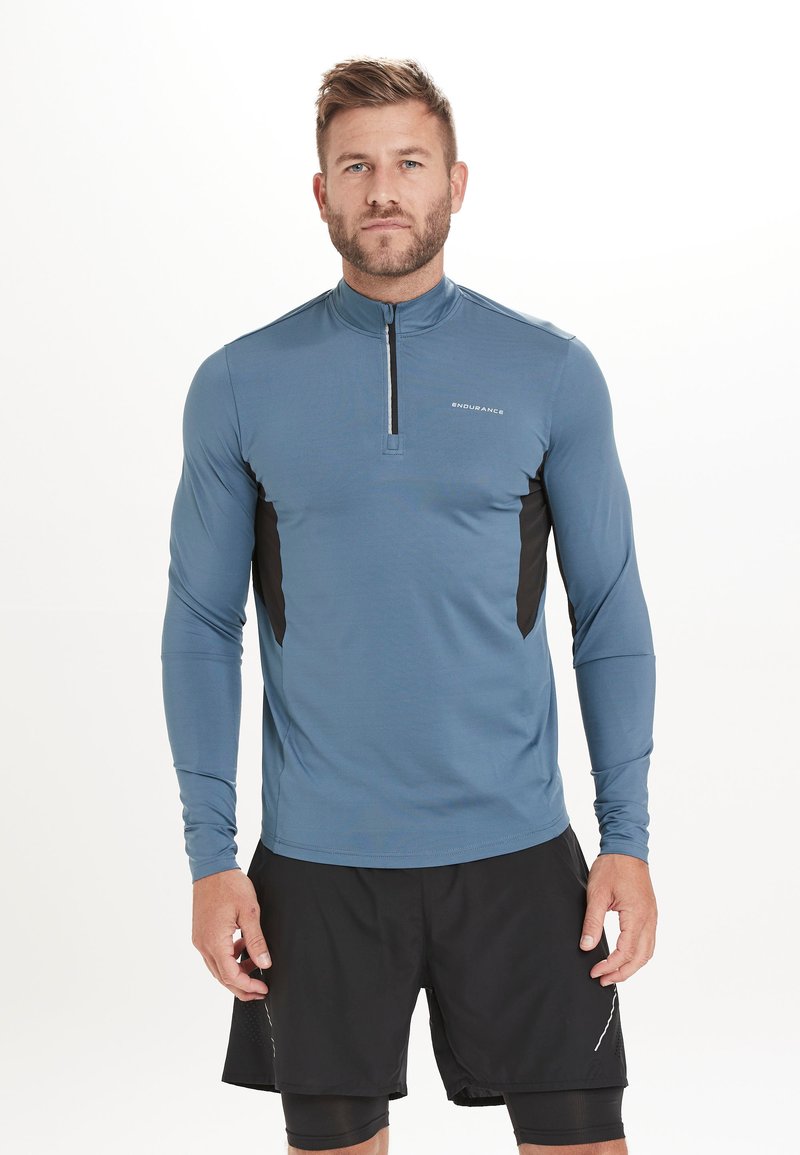 Langärmliges Sportshirt in Blau mit einem halben Reißverschluss an der Vorderseite, schwarzen seitlichen Einsätzen und einem glatten, feuchtigkeitsableitenden Stoff.