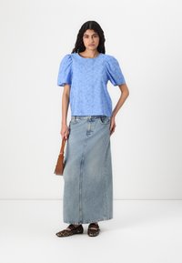 Haut texturé bleu clair avec des manches bouffantes, associé à une longue jupe en denim. Ballerines à imprimé léopard noir et marron, avec un sac à bandoulière marron.