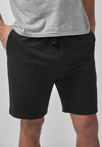 Shorts negri din bumbac, cu talie elastică și sistem de închidere cu șnur. Textură netedă, design până la genunchi, fără modele sau accente vizibile.