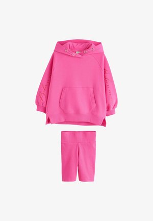 Kirkkaan pinkki huppari, jossa etutasku ja kiristysnyörit, yhdistetty samanlaiset polvenmittaiset leggingsit, molemmissa hillittyä brändäystä hihoissa ja lahkeessa.