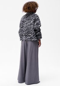 Zebra-print oversize jas met een hoge kraag en twee knopen aan de achterkant, gecombineerd met wijde grijze broeken in een textuurstof.