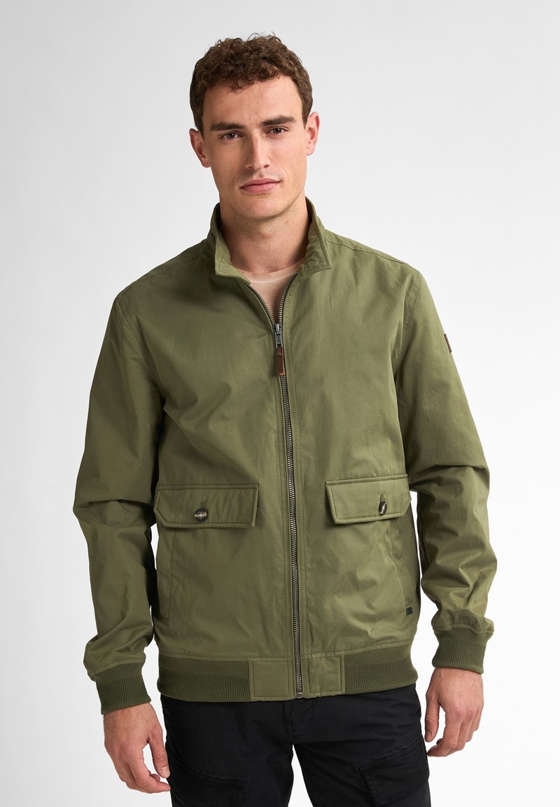 Jachetă bomber de culoare verde măsliniu, cu guler înalt, fermoar frontal și două buzunare cu clapă și nasturi. Include manșete și tiv din tricot.