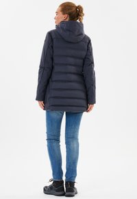 Mørkeblå pufferjakke med hætte, med horisontale kviltninger, en længere pasform og en glat tekstur. Sammen med lyseblå jeans og sorte støvler.
