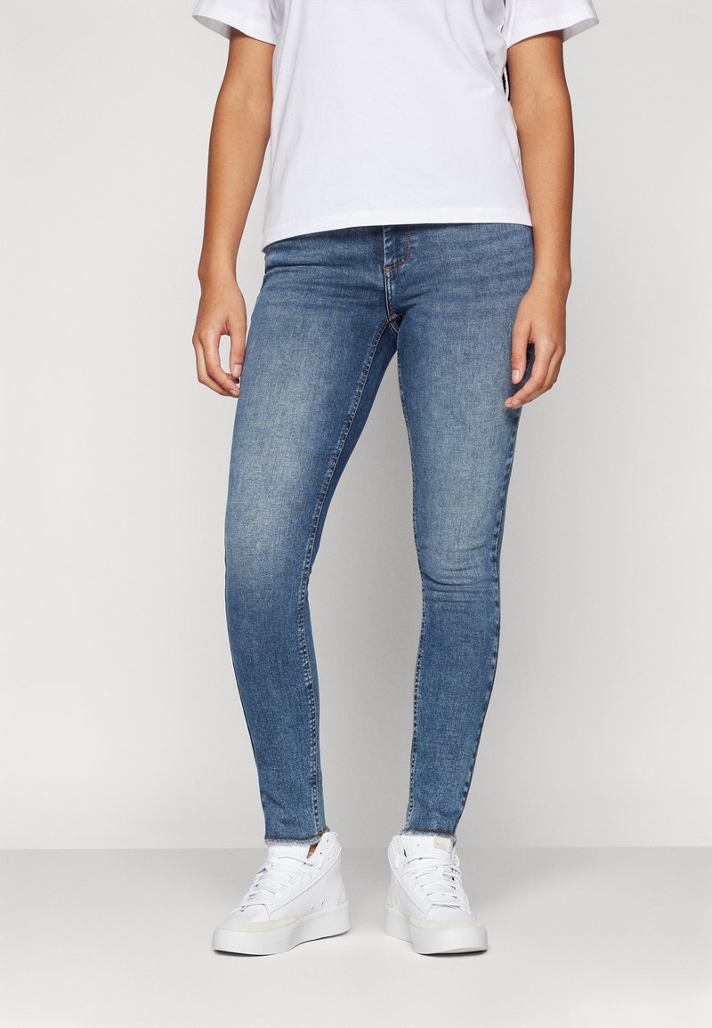 Blå smala jeans av denim, med en klassisk femficksdesign, en medelwash och en slät textur. Bärs med vita sneakers.