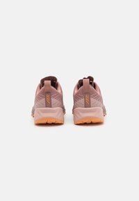 Lightweight hiking shoes in muted pink and gray tones, featuring textured material, reinforced heel, and a durable rubber sole with vibrant orange accents.