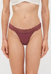 String bordeaux avec ceinture en dentelle florale, présentant un corps en coton lisse et un design à couverture minimale, mettant en valeur des bords et des détails délicats.