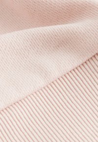 Ljust rosa stickad tyg som visar en slät, ribbad textur med horisontella linjer och fina sömnadsdetaljer.