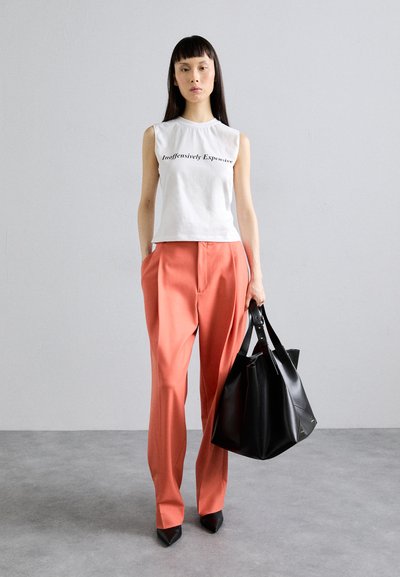 Sleeveless white cotton top with text, orange tailored pants, black pointed-toe shoes, and a structured black tote bag. Neutral background.