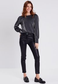 Zwarte, glanzende, getailleerde broek gecombineerd met een metallic lange mouwen top met een relaxte pasvorm en volumineuze mouwen.
