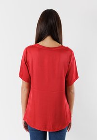 Blusa corta a maniche corte in raso rosso con scollo rotondo e orlo curvo, caratterizzata da una texture liscia e un sottile lucido.