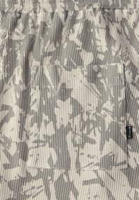 Szary i kremowy materiał z wąskich żeberek z teksturowaną powierzchnią z wzorem liści. Zawiera kieszeń naszywaną i małą metkę.