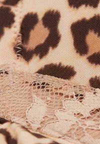 Tissu imprimé léopard en fauve et marron, agrémenté d'un délicat ourlet en dentelle beige avec des motifs floraux, créant une apparence texturée et superposée.